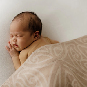 Newborn baby sleeping under a patterned blanket on a neutral background