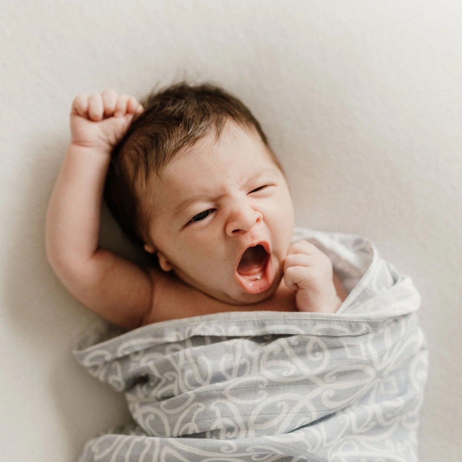 Newborn baby wrapped in a patterned blanket on a light background