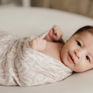 Baby wrapped in a patterned blanket lying on a soft surface