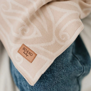 Beige textured blanket with a brand label on a blurred background