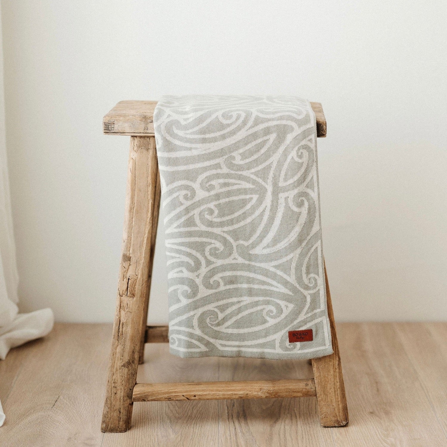 Patterned blanket draped over a wooden stool on a light wooden floor.