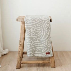Patterned blanket draped over a wooden stool on a light wooden floor.