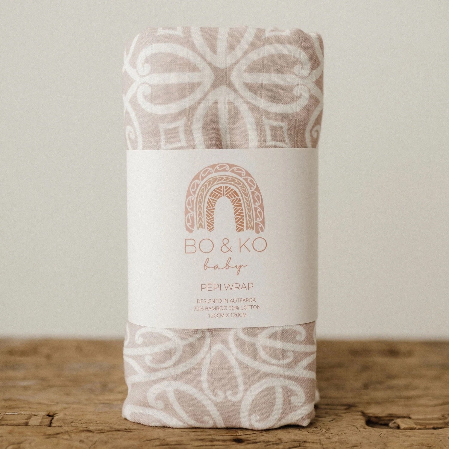 Folded baby wrap with a pattern and 'BO & KO baby' label on a wooden surface.