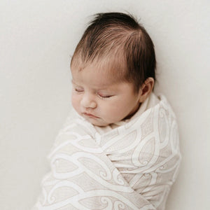 Newborn baby wrapped in a patterned blanket on a plain background