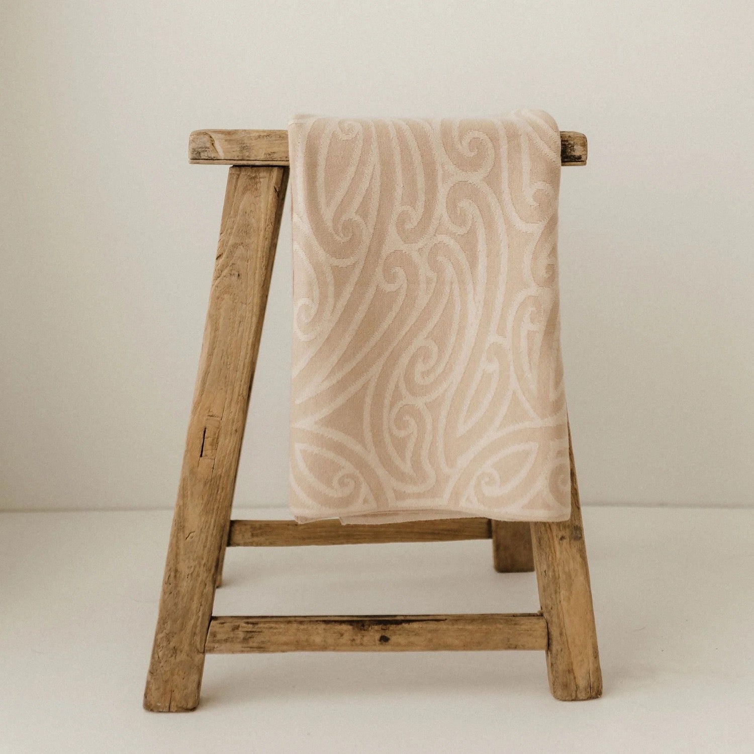 Patterned baby blanket draped over a wooden stool against a plain background