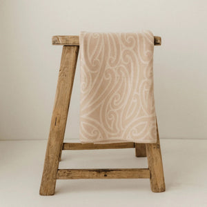 Patterned baby blanket draped over a wooden stool against a plain background