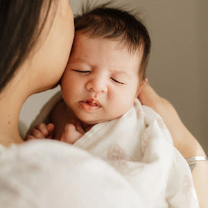 Newborn baby wrapped in a white muslin tiki print being held by an adult