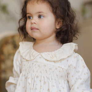 Young girl wearing a white dress with a floral pattern, standing outdoors.