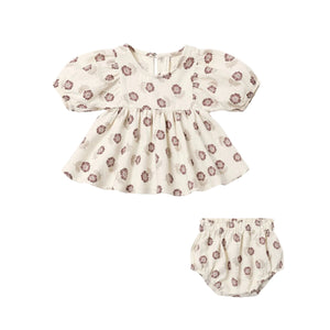 A baby girl's two-piece outfit set featuring a short-sleeve puff-sleeve smocked blouse and matching bloomers, both in a cream-colored cotton fabric with a brown floral pattern, shown on a plain white background.