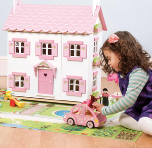 Le Toy Van Sophie's House, a beautiful two story pink and white dolls house, being played with by a young girl. Also pictured is Sophie's Car